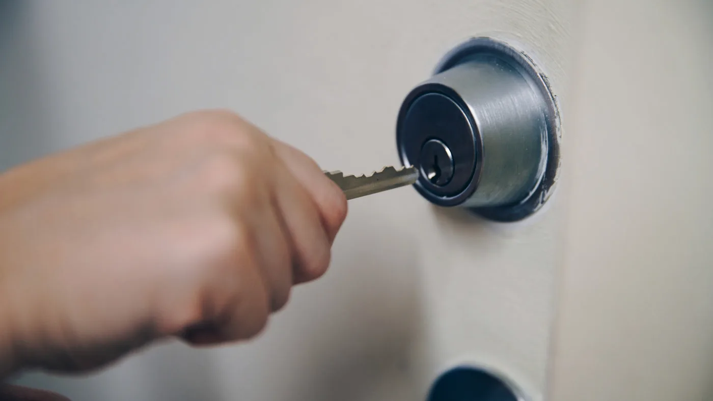 A hand turning a key in a front door lock